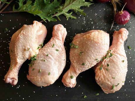 Four organic pastured chicken drumsticks arranged side by side.