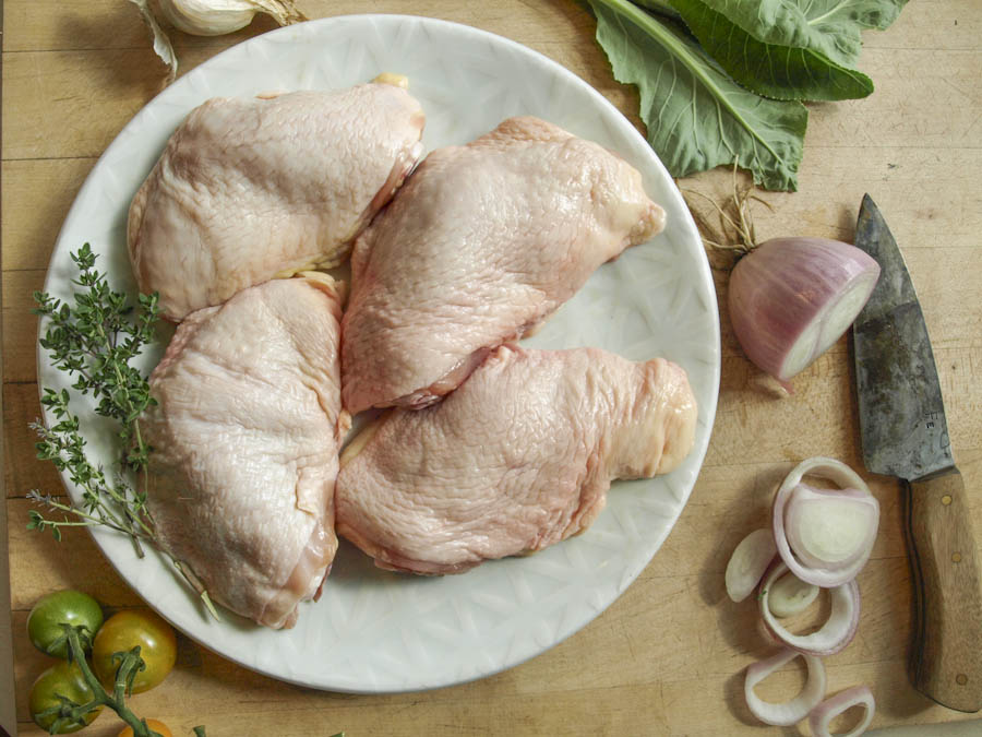 organic pastured chicken thighs on a plate with fresh veggies arrangement.