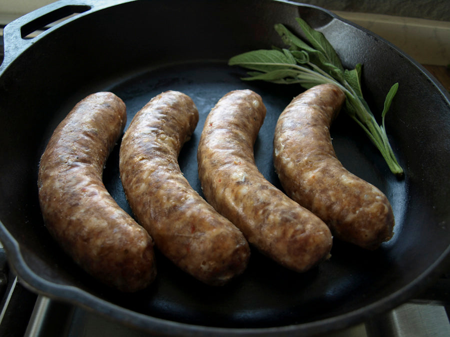 Four links of hot italian sausage with sage, in a cast iron pan.