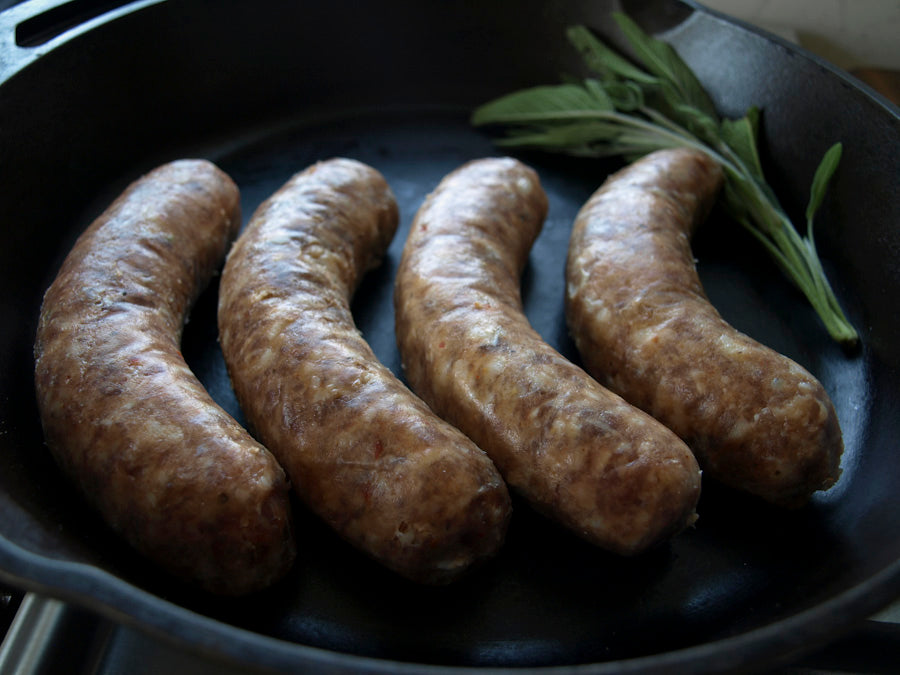 Four links of mild Italian sausage, made with pastured pork, on a cast iron skillet.